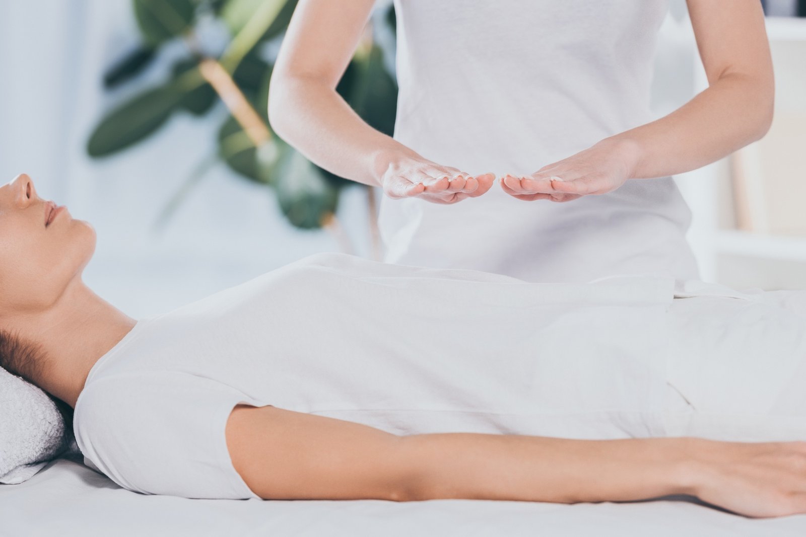 cropped shot of calm young woman receiving reiki healing treatment on stomach